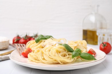 Delicious pasta with brie cheese, tomatoes and basil leaves on white tiled table, closeup. Space for text