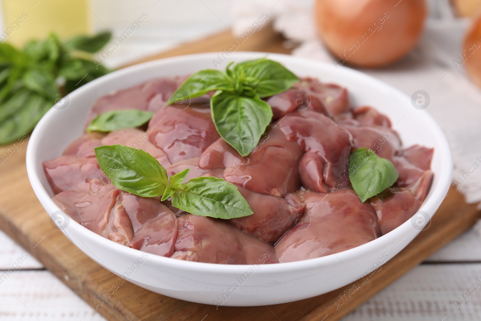 Photo of Bowl with raw chicken liver and basil on white wooden table, closeup