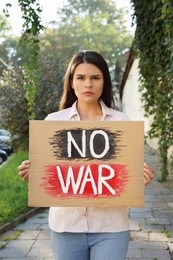 Photo of Sad woman holding poster with words No War outdoors