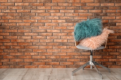 Photo of Fuzzy pillows on armchair near brick wall