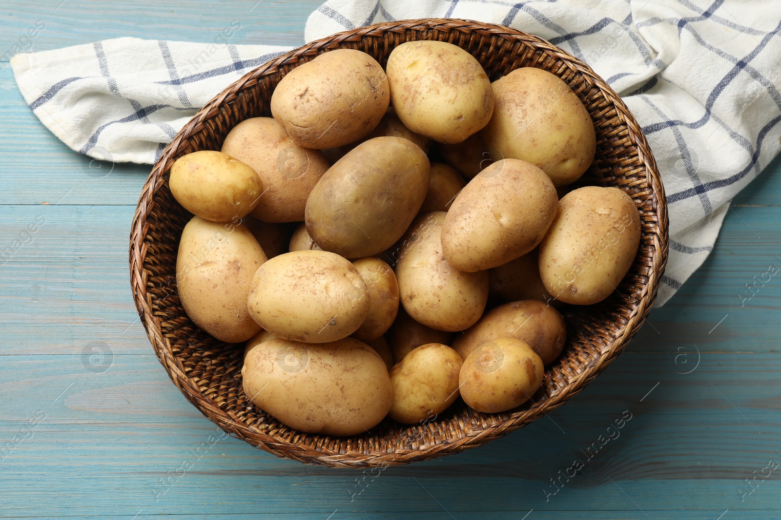 Photo of Raw fresh potatoes in wicker basket on light blue wooden table, top view