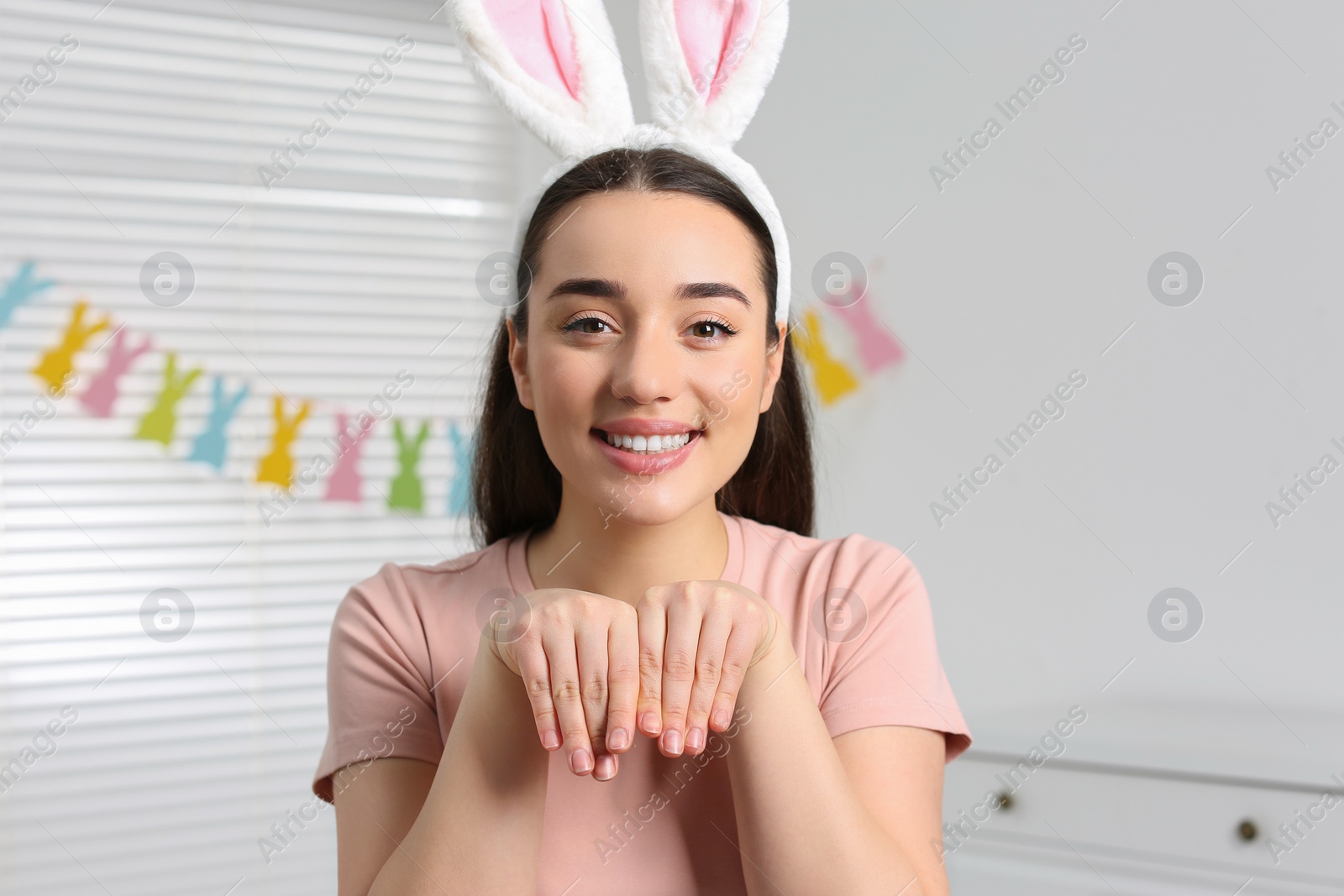 Photo of Happy woman wearing bunny ears headband in decorated room. Easter celebration