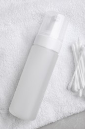 Photo of Bottle of face cleansing product and cotton buds on white towel, flat lay. Space for text