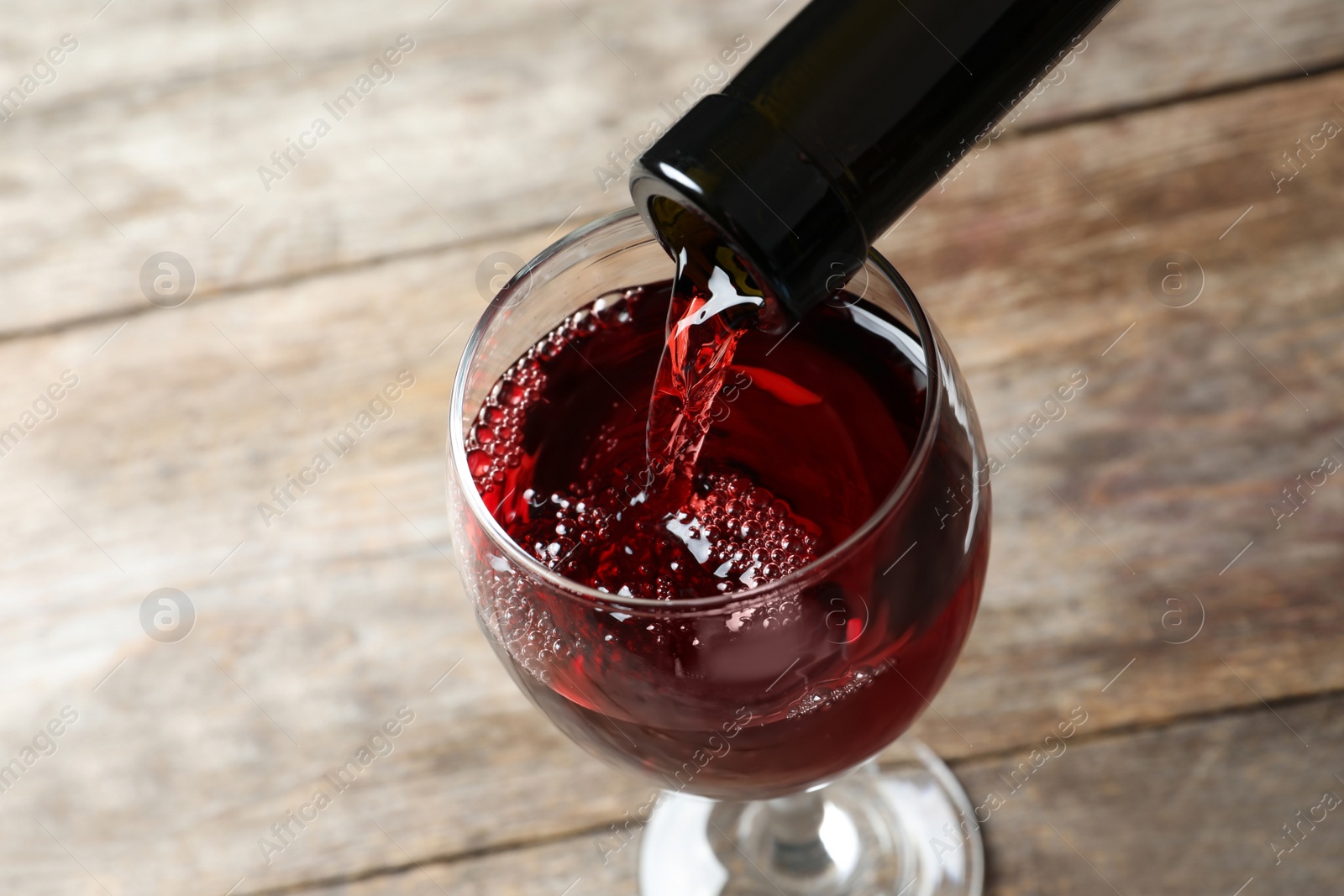 Photo of Pouring delicious red wine into glass on wooden background
