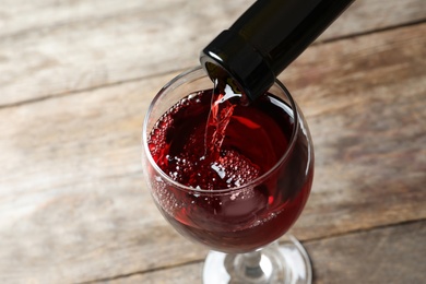 Photo of Pouring delicious red wine into glass on wooden background