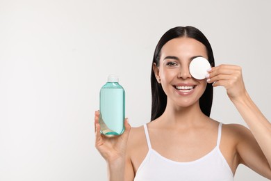 Photo of Young woman with micellar water and cotton pad on light grey background, space for text