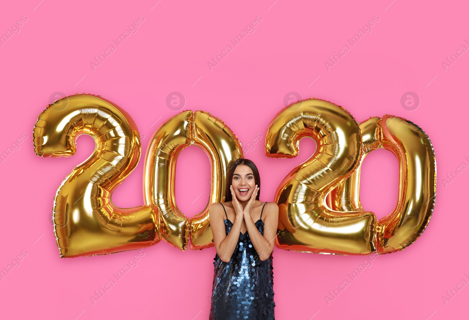 Photo of Excited young woman near golden 2020 balloons on pink background. New Year celebration