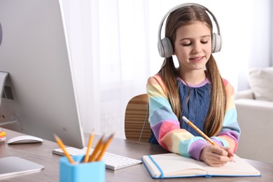 E-learning. Cute girl taking notes during online lesson at table indoors