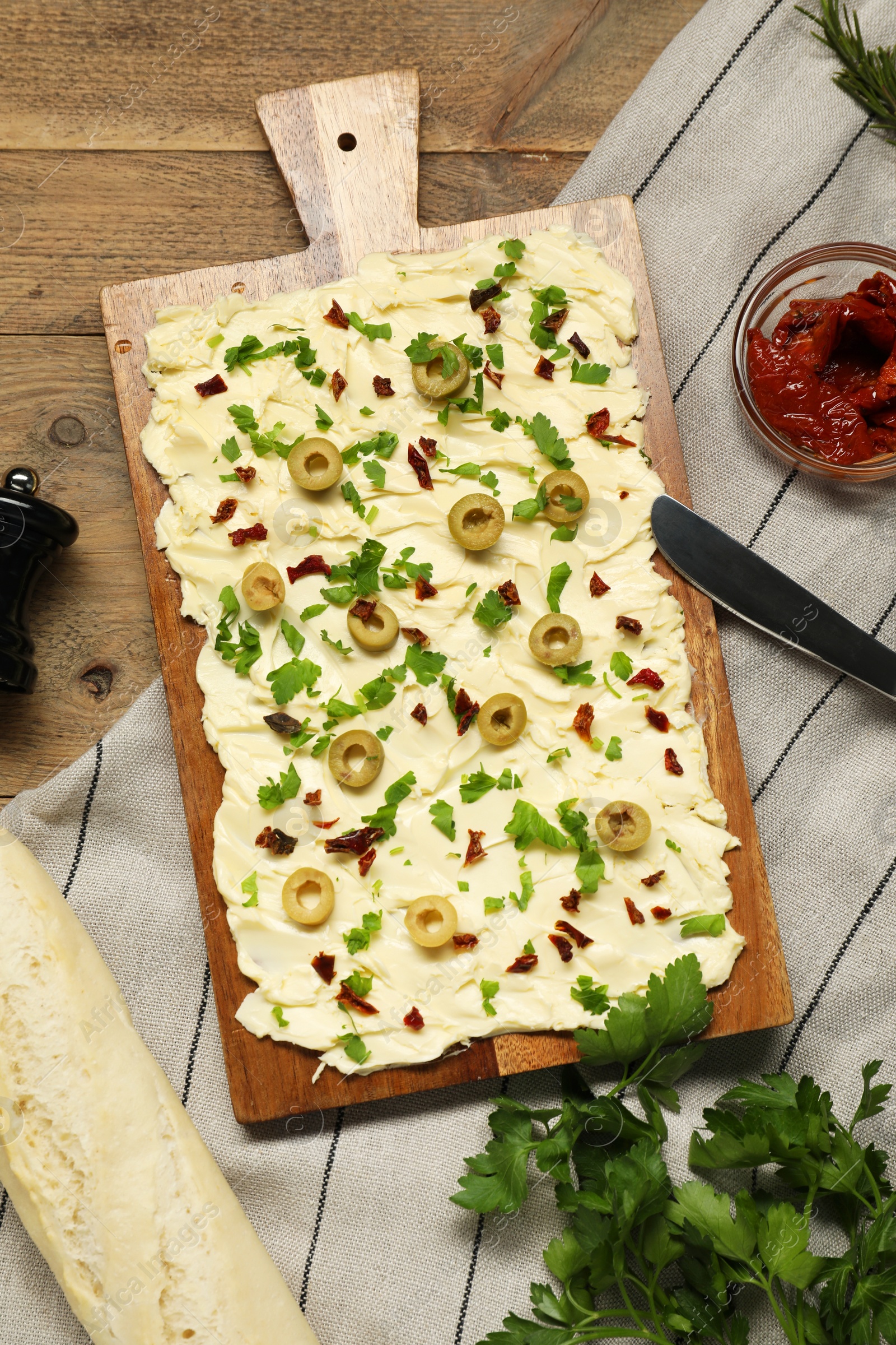 Photo of Fresh butter board with cut olives, sun-dried tomatoes, bread and knife on wooden table, flat lay