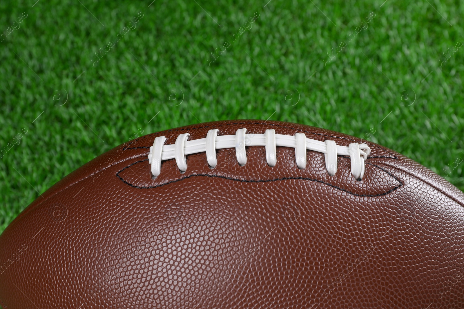 Photo of American football ball on green grass, closeup