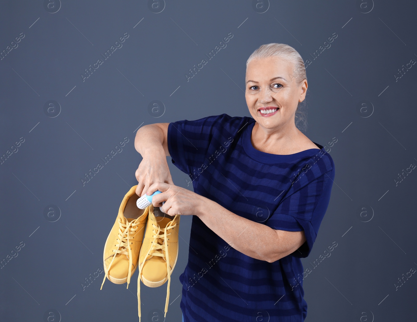 Photo of Woman putting capsule shoe freshener in footwear on color background