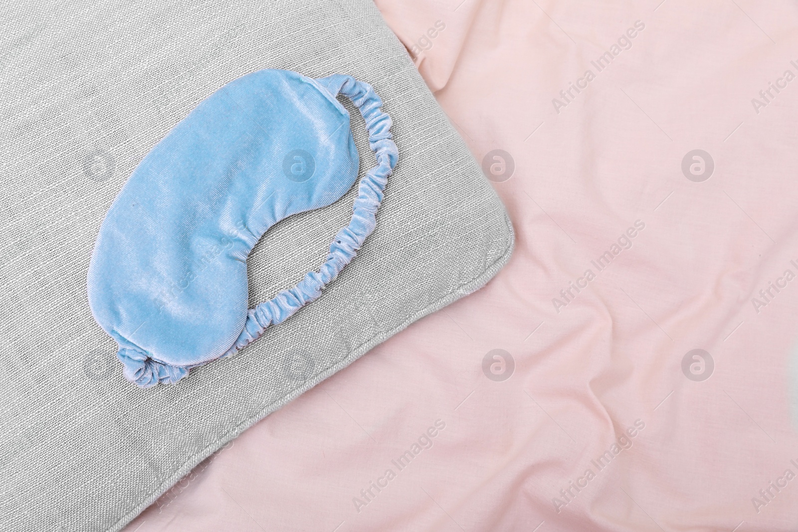 Photo of Light blue sleep mask on beige cloth, top view. Space for text