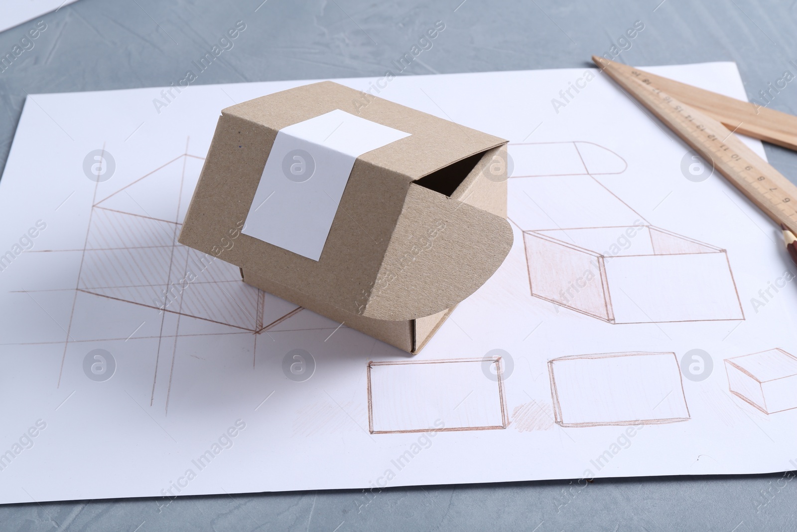 Photo of Creating packaging design. Drawing, box and ruler on blue textured table, closeup