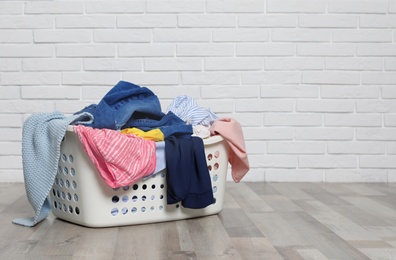 Photo of Laundry basket with dirty clothes on floor near brick wall. Space for text
