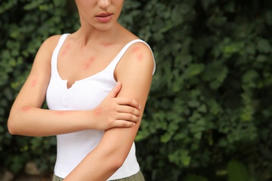 Photo of Woman scratching arm with insect bites in park, closeup. Space for text