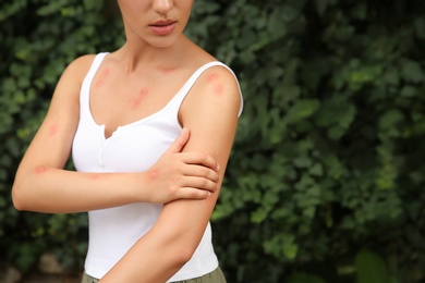 Woman scratching arm with insect bites in park, closeup. Space for text