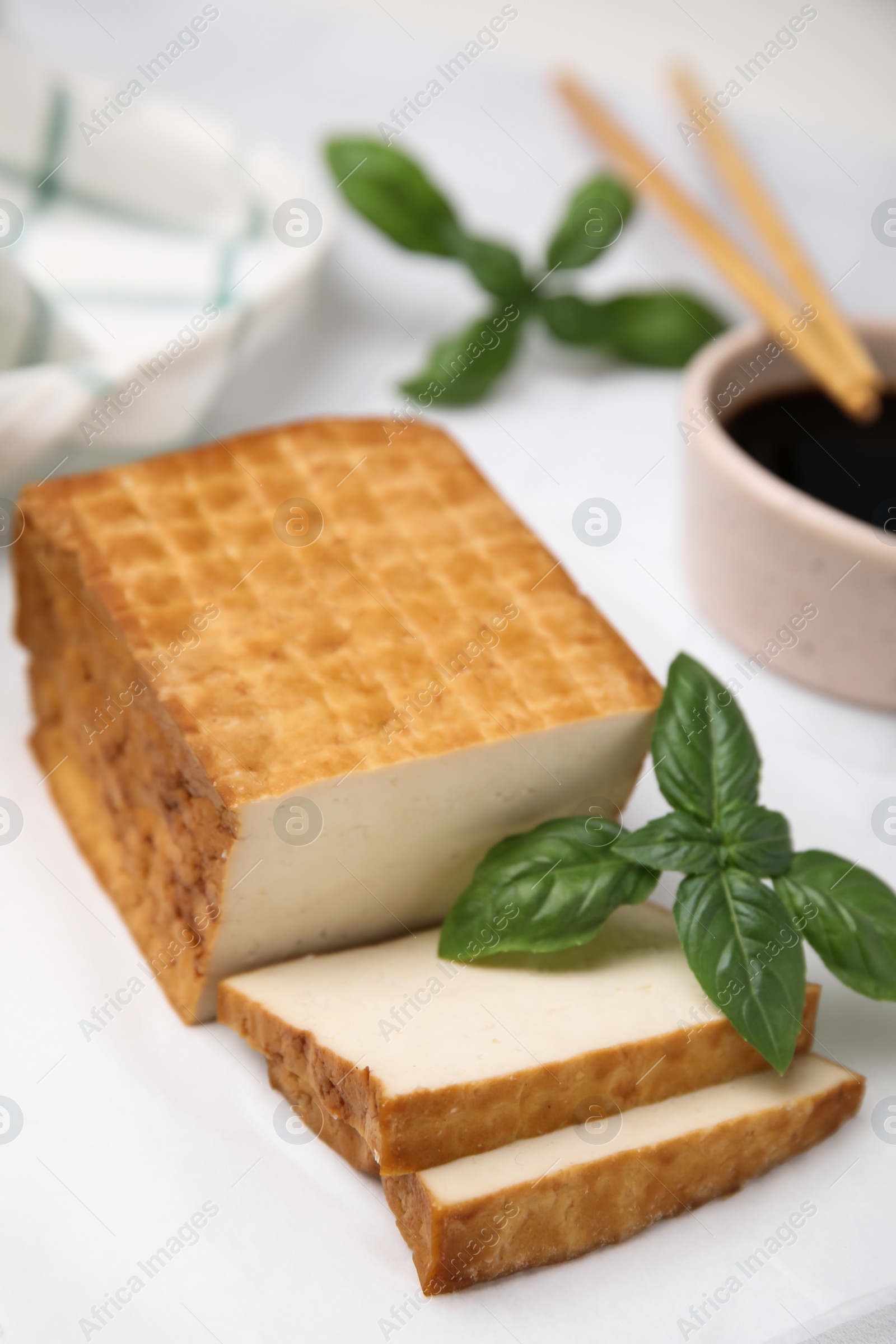 Photo of Delicious smoked tofu and basil on tiled table, closeup