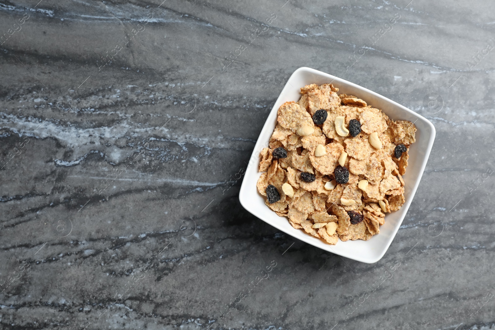 Photo of Bowl of cornflakes and raisins on dark table, top view with space for text. Whole grain cereal for breakfast