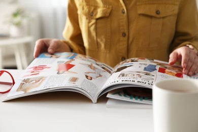 Woman reading fashion magazine at white table indoors, closeup