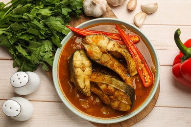 Photo of Tasty fish curry and ingredients on white wooden table, flat lay. Indian cuisine