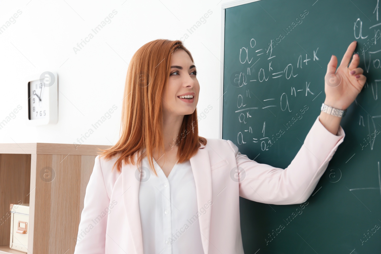 Photo of Beautiful young teacher explaining math formulas written on blackboard in classroom