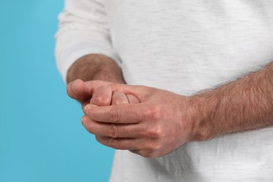 Photo of Man cracking his knuckles on light blue background, closeup. Bad habit