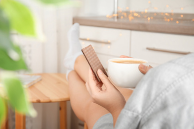 Photo of Woman having delicious wafer and coffee for breakfast indoors, closeup