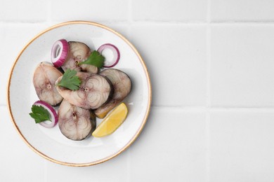 Photo of Slices of tasty salted mackerel with lemon and onion on white tiled table, top view. Space for text