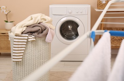 Photo of Laundry basket overfilled with clothes near washing machine in bathroom