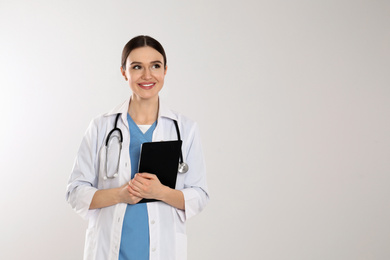Doctor with stethoscope and clipboard on light grey background. Space for text