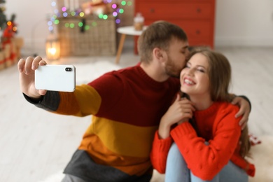 Photo of Happy young couple taking selfie in decorated for Christmas room