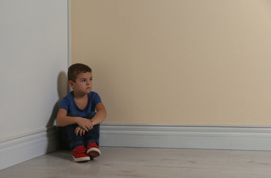 Photo of Little boy sitting in corner near yellow wall, space for text. Child in danger