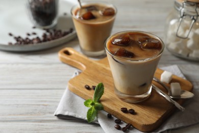 Photo of Delicious iced coffee with milk, beans and mint on white wooden table, space for text