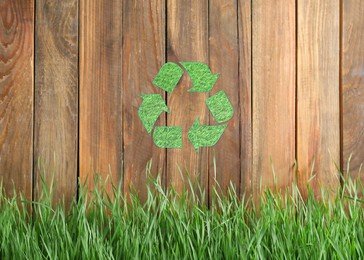 Image of Green grass and illustration of recycling symbol on wooden fence