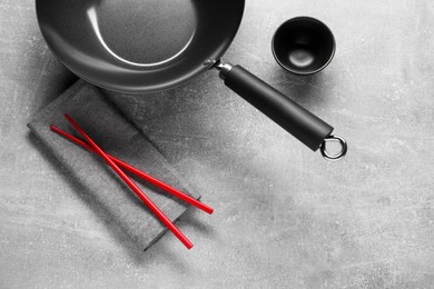 Photo of Empty iron wok, sauce bowl and chopsticks on grey table, flat lay