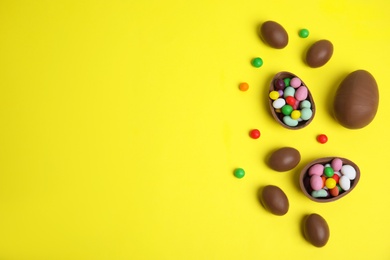 Photo of Tasty chocolate eggs and colorful candies on yellow background, flat lay. Space for text