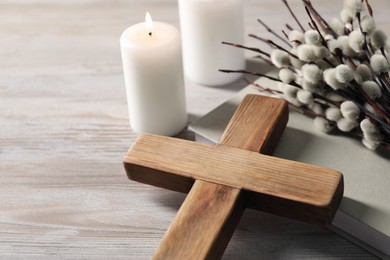 Photo of Burning candles, cross, book and willow branches on wooden table, closeup