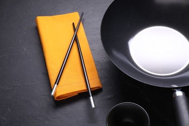 Photo of Empty iron wok, sauce bowl and chopsticks on black table, closeup