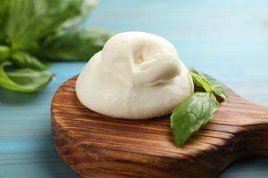 Photo of Delicious burrata cheese with basil on light blue wooden table, closeup
