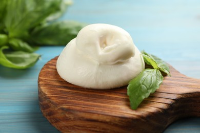 Photo of Delicious burrata cheese with basil on light blue wooden table, closeup