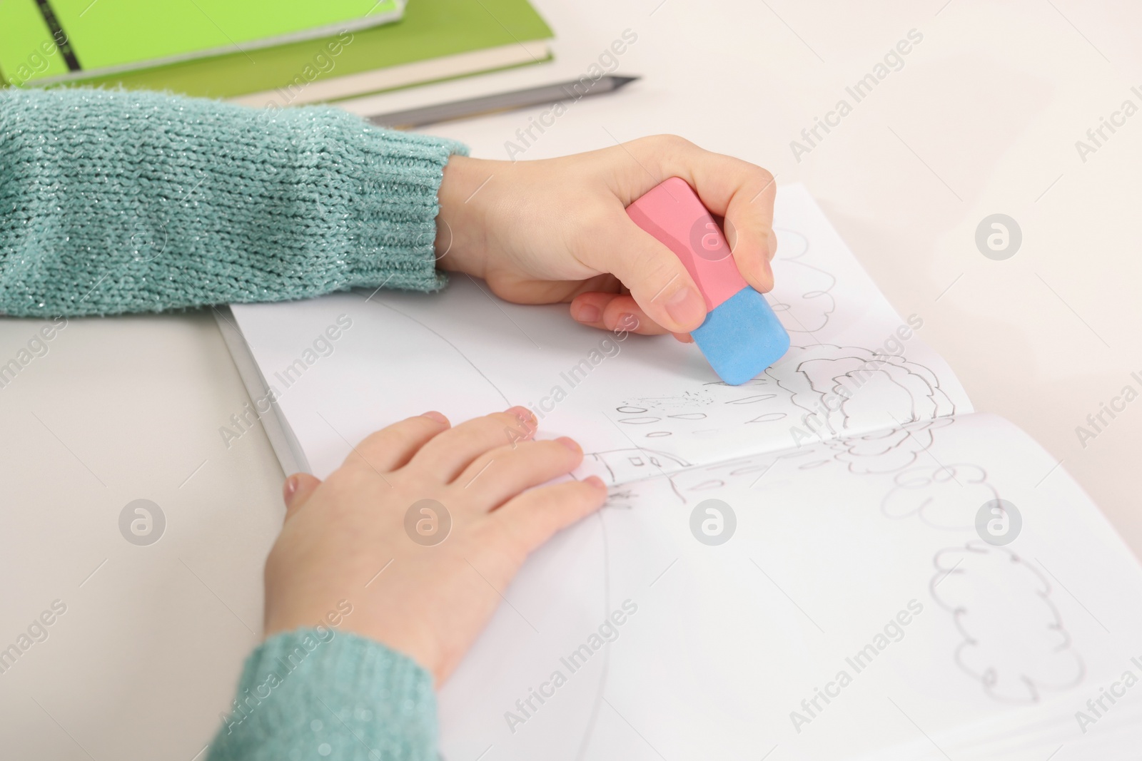 Photo of Girl erasing drawing in her book at white desk, closeup