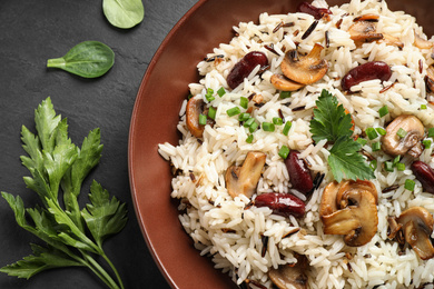 Photo of Delicious rice pilaf with mushrooms and beans on black table, closeup