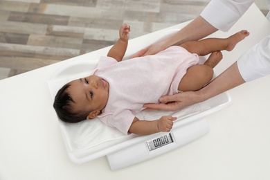 Photo of Doctor weighting African-American baby on scales indoors, above view