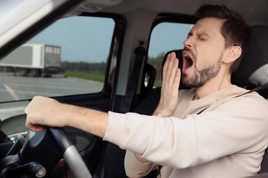Photo of Sleepy man yawning while driving his car