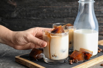 Photo of Woman taking glass of milk with coffee ice cubes from board on table