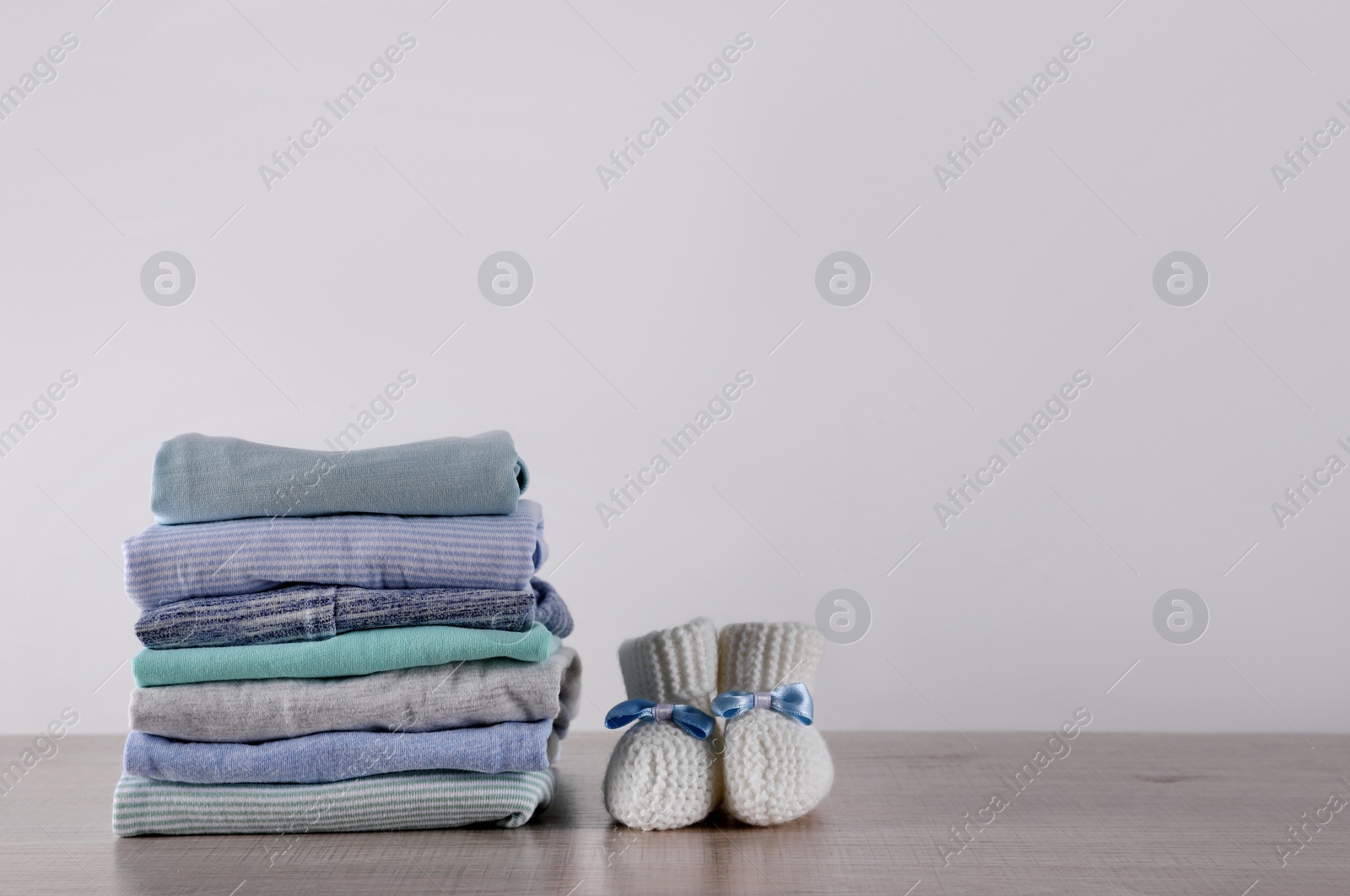 Photo of Stack of baby boy's clothes and booties on wooden table against white background, space for text