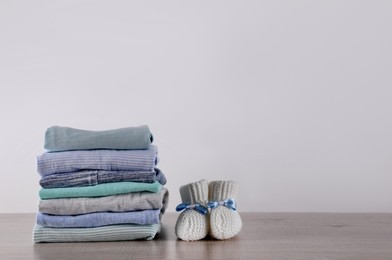 Photo of Stack of baby boy's clothes and booties on wooden table against white background, space for text