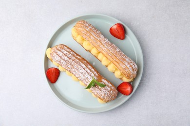 Photo of Delicious eclairs filled with cream, strawberries and mint on light table, top view