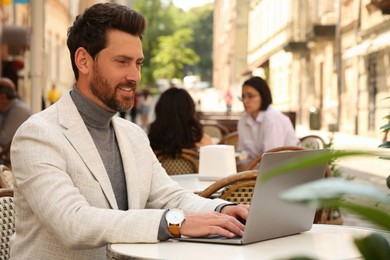 Photo of Man working on laptop at table in outdoor cafe