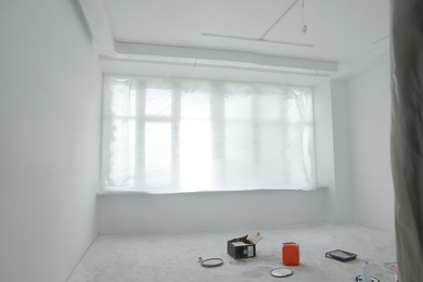 Photo of Window covered with plastic film and tools on floor in room